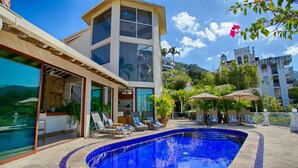 Un hotel moderno con piscina, sillas de descanso y vistas del paisaje circundante.