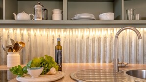 Een keuken met een roestvrijstalen spoelbak, een houten snijplank met groenten, een fles olie en een witte kom.