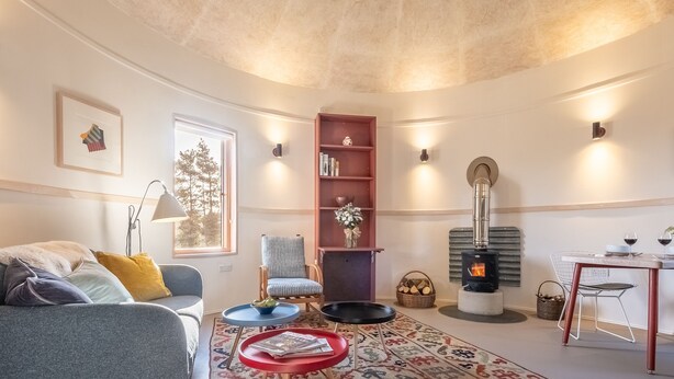 Een gezellige woonkamer met een open haard, een bank, een stoel, een bijzettafeltje en een boekenkast.