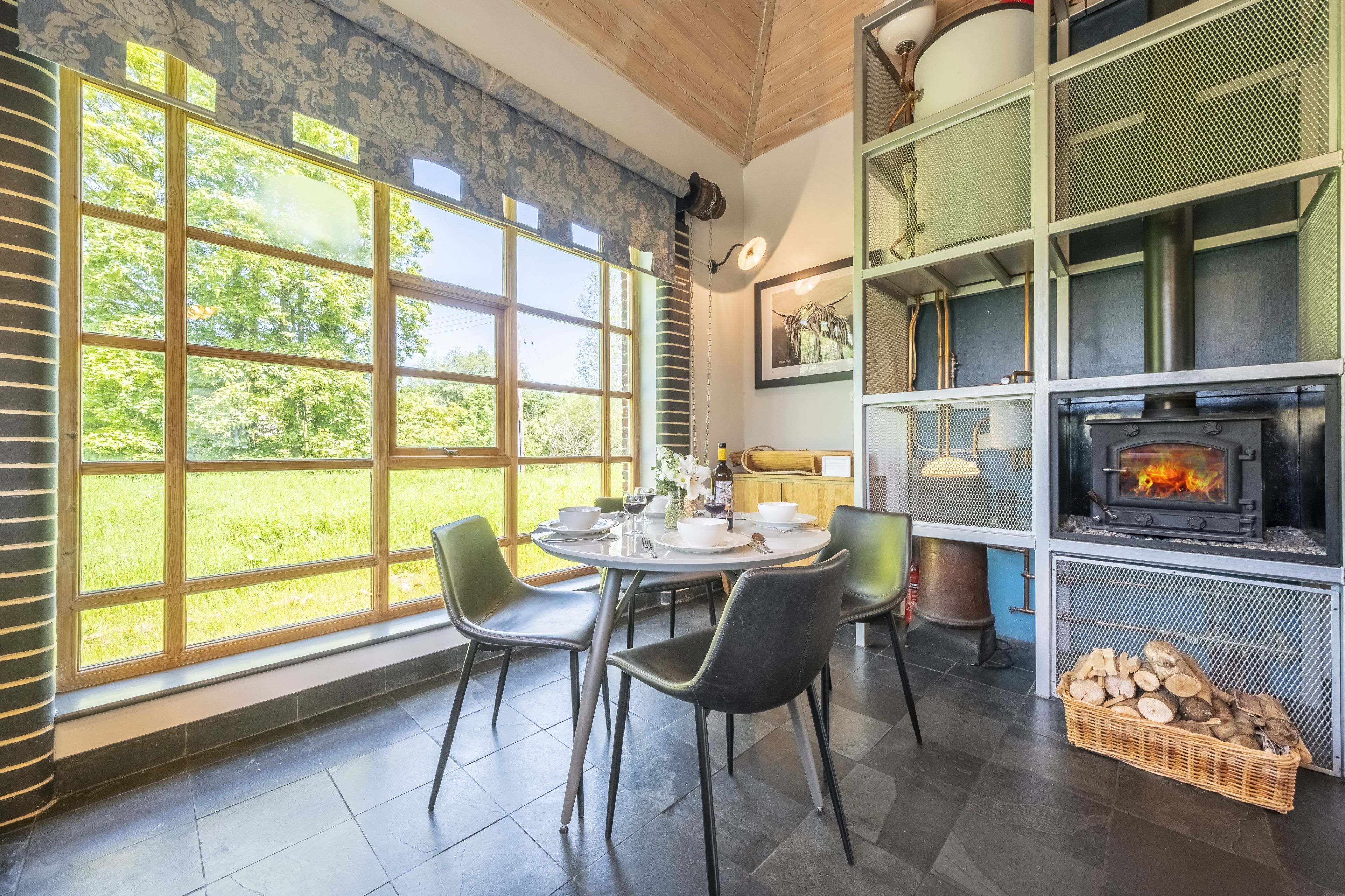 A dining area with a large window, a fireplace, and a collection of items on shelves.