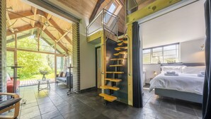A modern hotel room with a large bed, a wooden staircase, and a balcony with a view of greenery. - Ultimate Constable Country retreat -The Pump House (Colchester)