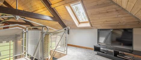 A high-ceilinged attic room with a skylight, a staircase with metal railings, and a TV stand with a flat-screen TV.