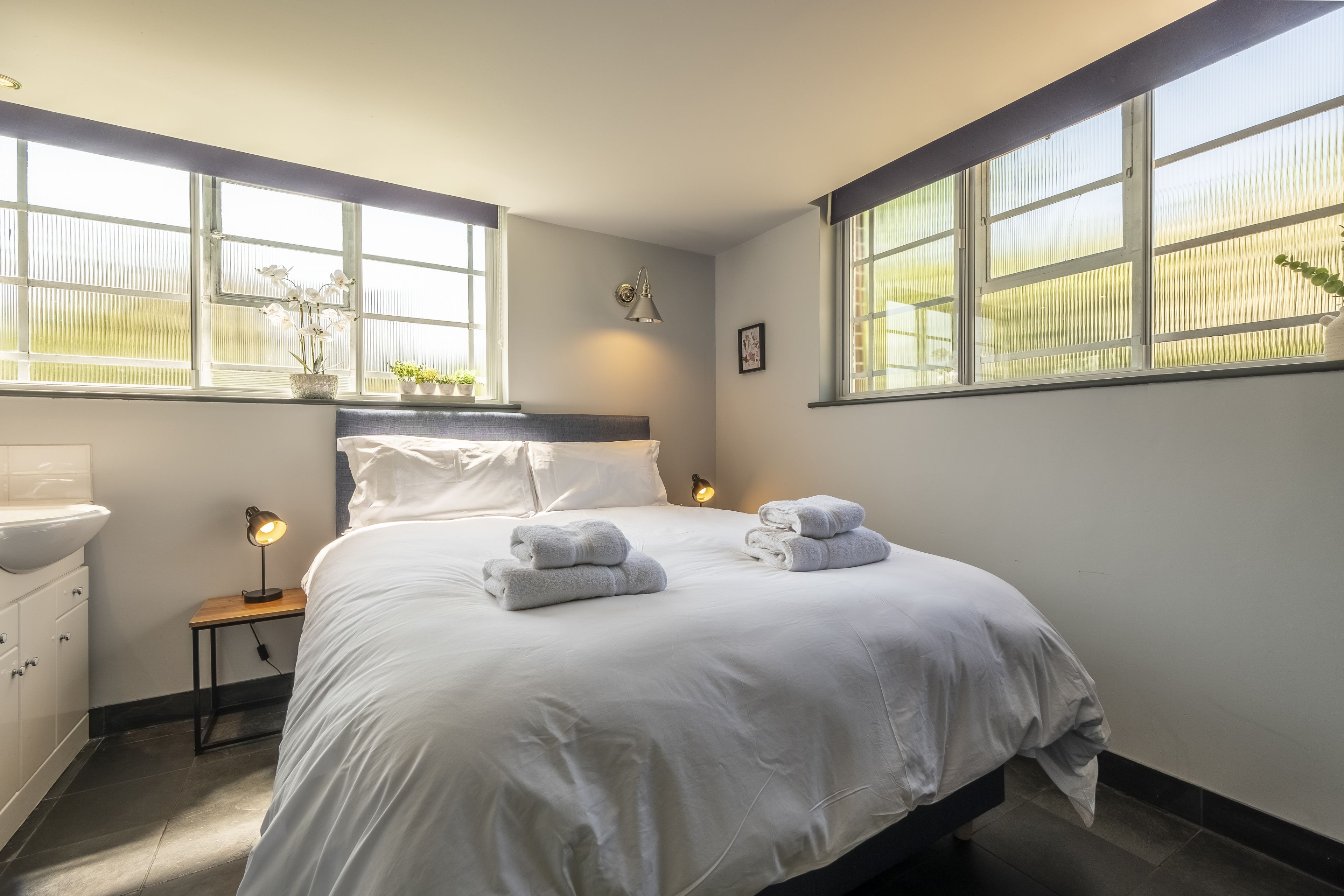 Un dormitorio con una cama grande, dos mesitas de noche, una lámpara de pared y una ventana con persianas.
