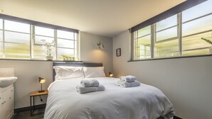 Ein Schlafzimmer mit einem großen Bett, zwei Nachttischen, einem Beistelltisch, einem Fenster mit Jalousien und einer Wandlampe.