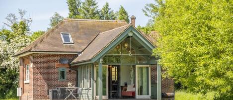 A small brick house with a covered porch, a dining table, and a red sofa.