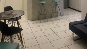 A compact kitchen with a microwave, a coffee maker, and a small countertop. There are two stools and a table with a woven placemat. - Ponta Negra Beach EFM - 323 (Natal)