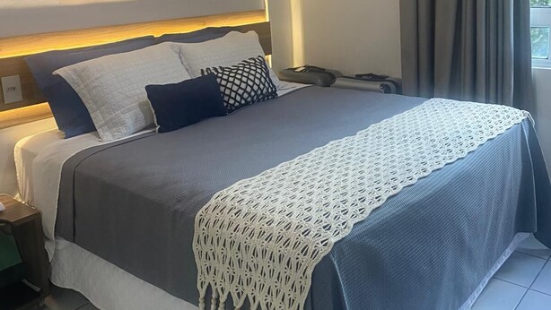 A neatly made bed with a grey and white bedspread, a macrame throw, and a geometric wall art piece above it. - Ponta Negra Beach EFM - 323 (Natal)