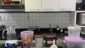 A kitchen counter with various items including a coffee maker, containers labeled 'Açúcar' and 'Café', a Snob brand bag, and a wooden tray. - Ponta Negra Beach EFM - 323 (Natal)