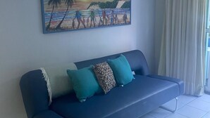 A blue sofa with teal cushions, a painting of a beach scene, and a white air conditioning unit on the wall. - Ponta Negra Beach EFM - 323 (Natal)