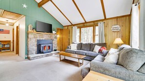 A cozy living room with a stone fireplace, a grey sofa, and a wooden ceiling.