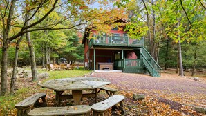 A rustic cabin with a balcony, surrounded by trees and a picnic table with benches.