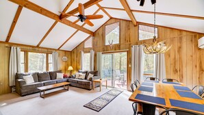 A spacious living area with a large wooden dining table, a sofa, and a ceiling fan.