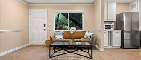 A living room with a sofa, coffee table, and a kitchen area with appliances.