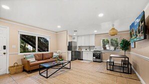 A modern kitchen with white cabinets, a stainless steel refrigerator, and a dining area with a small table and chairs.