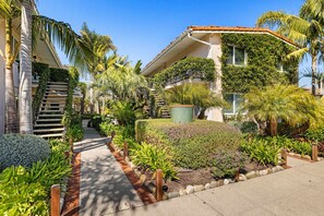 A residential building with a covered staircase, a garden with various plants, and a clear blue sky. - Surf Station #3 | 1BR Walk to Beach & Funk Zone (Santa Barbara)