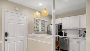 A kitchen with white cabinets, a stainless steel refrigerator, a dishwasher, and two hanging pendant lights.