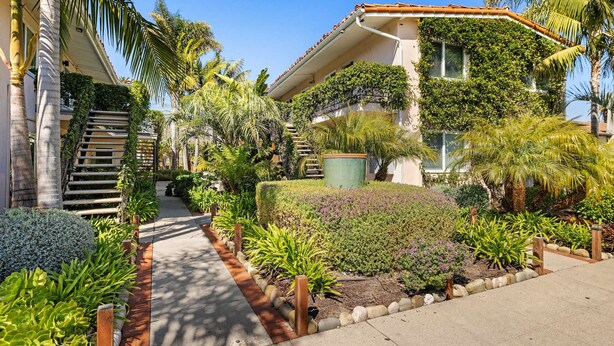 A residential building with a covered staircase, lush garden, and palm trees.