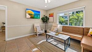 A living room with a sofa, chairs, a coffee table, a ceiling fan, and a large window with a view of greenery.