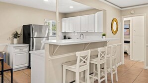 A kitchen with white cabinets, a stainless steel refrigerator, a white island with bar stools, and a gold mirror on the wall.