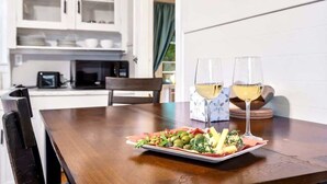Ein Esstisch mit einer Speisenplatte und zwei Gläsern Weißwein, einer Mikrowelle sowie einem Schrank mit Geschirr im Hintergrund.