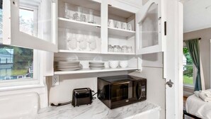 Eine kompakte Küche mit integriertem Mikrowellenherd, einem Toaster und Regalen mit Gläsern und Geschirr.