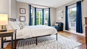 Ein Schlafzimmer mit Bett, Nachttisch, Stuhl und einem Fenster mit Vorhängen.