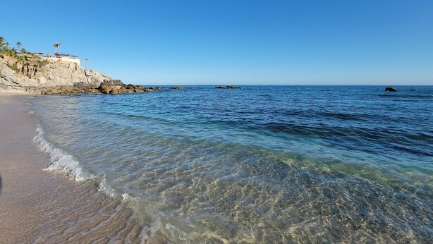 A beach with clear water, a rocky cliff, and a few umbrellas. - MILLION DOLLAR VIEW PENTHOUSE 2BDR, 2 BTH  (Cabo San Lucas)