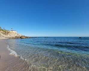 A beach with clear water, a rocky cliff, and a few umbrellas.