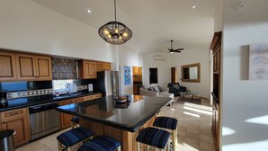 A spacious kitchen with wooden cabinets, a stainless steel refrigerator, and a central island with bar stools. - MILLION DOLLAR VIEW PENTHOUSE 2BDR, 2 BTH  (Cabo San Lucas)