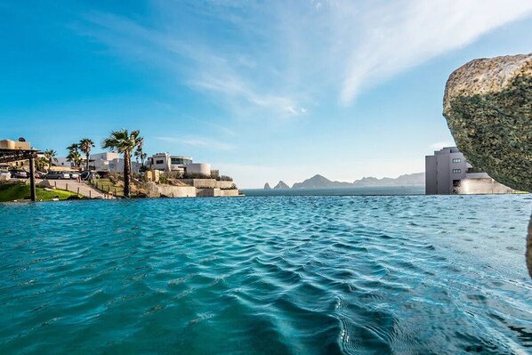 A coastal view with a rocky outcrop, buildings, and palm trees.