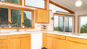 A modern kitchen with wooden cabinets, a white dishwasher, and large windows offering a view of greenery. - Gorgeous mountain view - 3 minutes from Downtown Asheville (Asheville)