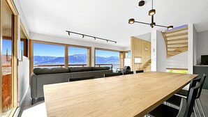 Et moderne køkken med et træbord, indbyggede siddepladser og store vinduer med udsigt til et bjerglandskab.