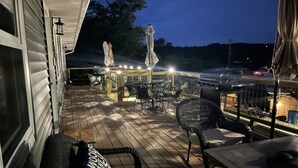 A deck with outdoor furniture, a grill, and a view of the surrounding area at night. - Deer Ridge Duplex - Beautiful Lake View with Shared Dock! (Sunrise Beach)