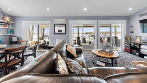 A spacious living room with a leather sofa, a dining area with a table and chairs, and a view through large sliding glass doors to an outdoor patio area.