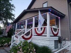 Welcome to this charming home, featuring a covered porch with a white railing and a patriotic theme.