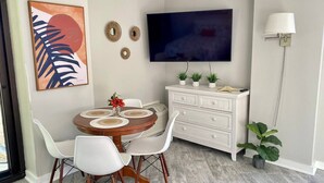 Un comedor con una mesa redonda, sillas blancas, un armario blanco y un televisor de pantalla plana montado en la pared.