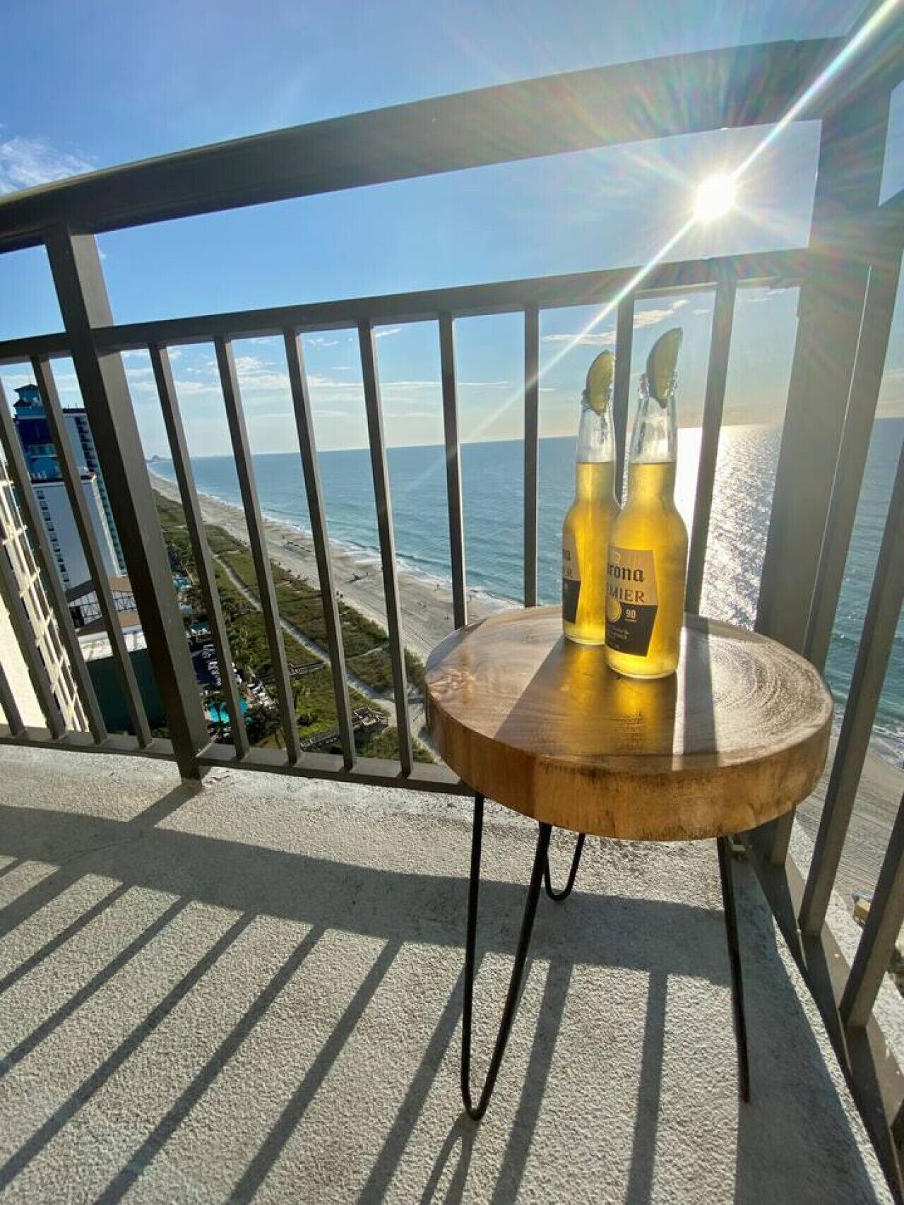 En balkon med udsigt over strand og hav, med to flasker Corona øl på et lille rundt bord.