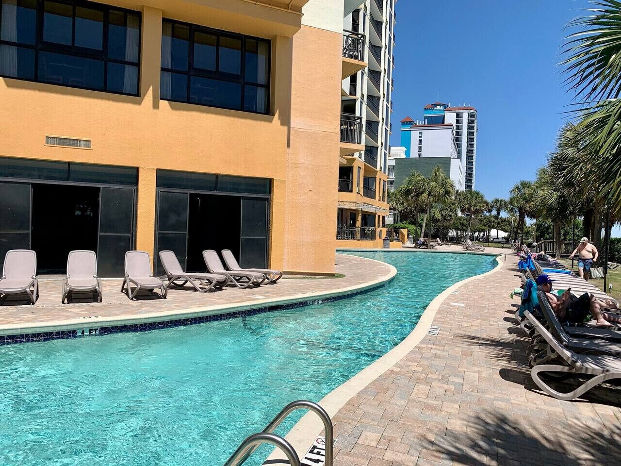 A swimming pool with lounge chairs and a building with multiple floors and balconies.