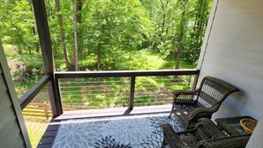 Une terrasse en bois avec une rambarde, des chaises en osier et un tapis à motifs.