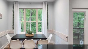 Un espace repas comprenant une table, des chaises, un panneau sur le mur et une fenêtre avec des rideaux.