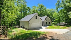 Une maison à deux étages avec un garage, entourée d’une zone boisée.