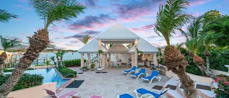 A resort pool area with lounge chairs, a gazebo, and a view of the sea.