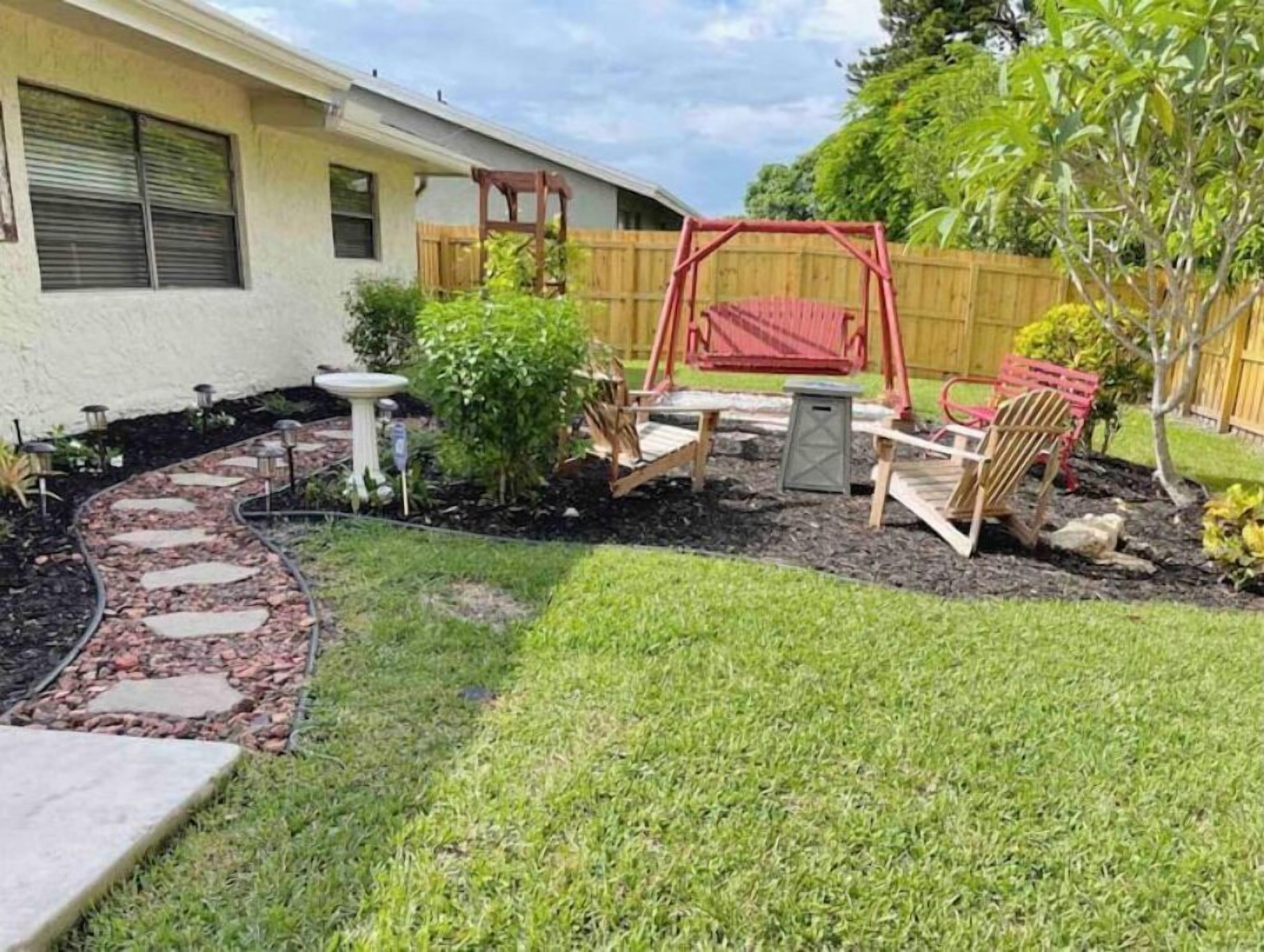 Un patio trasero con un tobogán, un pequeño jardín con piedras para caminar y una cerca de madera.