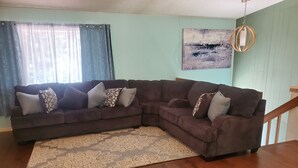 A living room with a brown sectional sofa, patterned rug, wooden flooring, and a staircase. - Lake Delton ~ Wisconsin Dells Home Provides Comfort and Access to All Activities (Wisconsin Dells)