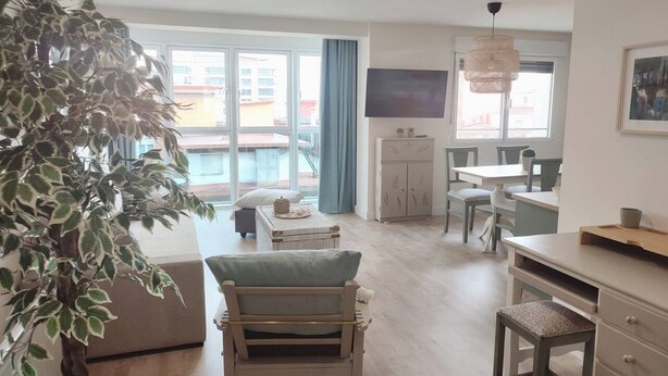 Ein Wohnzimmer mit großem Fenster, Essbereich, Fernseher und einer Pflanze.