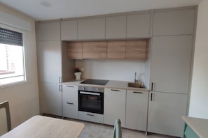 A compact kitchen with a built-in oven, a sink, and a window with blinds. - 178A Mar de Gijón: Apartment with Views by R2R (Gijón)