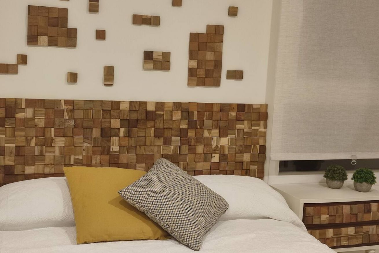 A bed with a white headboard, a yellow pillow, and a checkered pillow.
