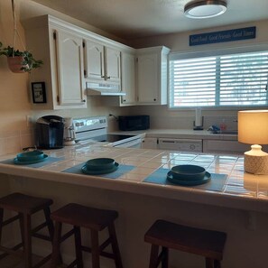 A kitchen with white cabinets, a microwave, a coffee maker, and a window with blinds.