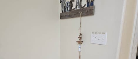 Una esquina de una habitación con una cesta tejida, una lámpara fijada a la pared y un letrero decorativo que dice 'BEAC'.