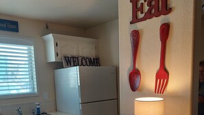 Una cocina con un cartel que dice 'Welcome', un refrigerador, un lavamanos y una mesa con un tazón y una lámpara.